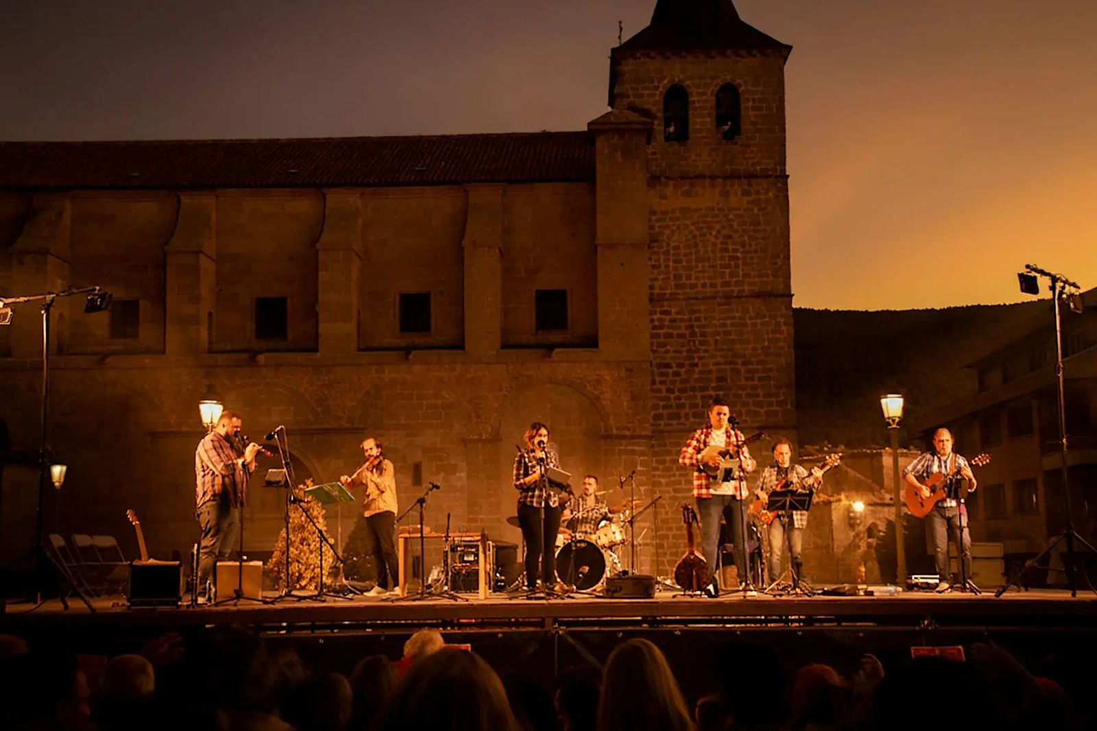 Ad Folkitum actuando al anochecer en un escenario frente a una iglesia de piedra, con el público en primer plano